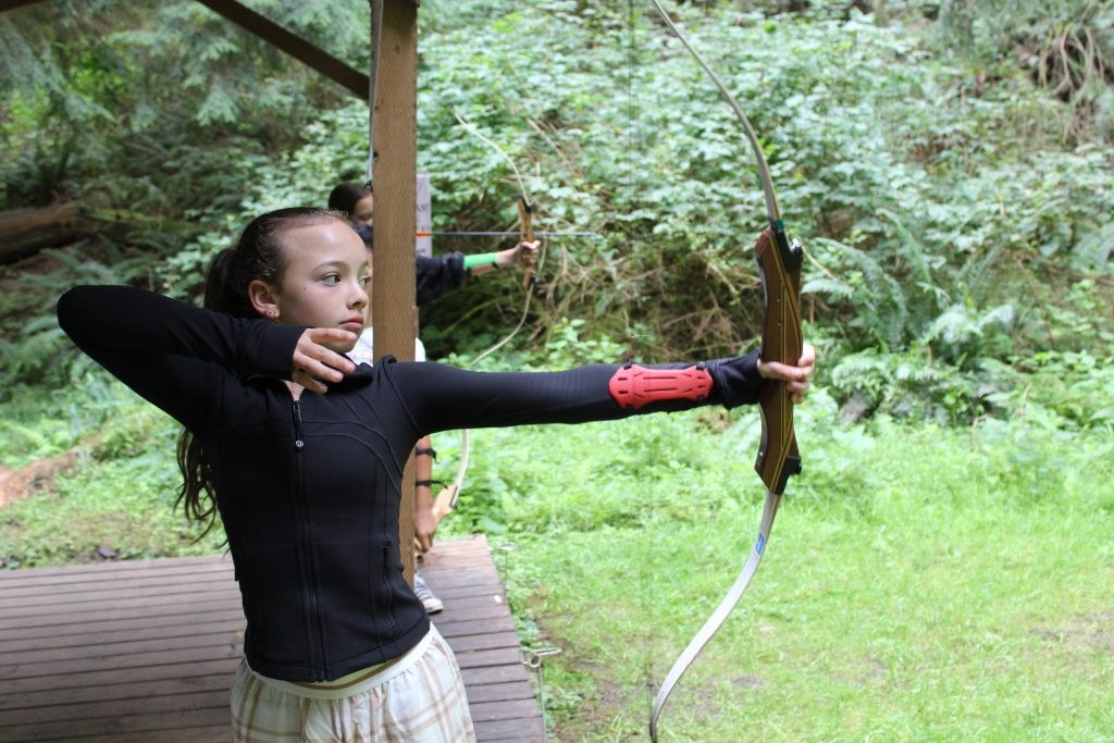 A camper aims a bow at the woodland archery range