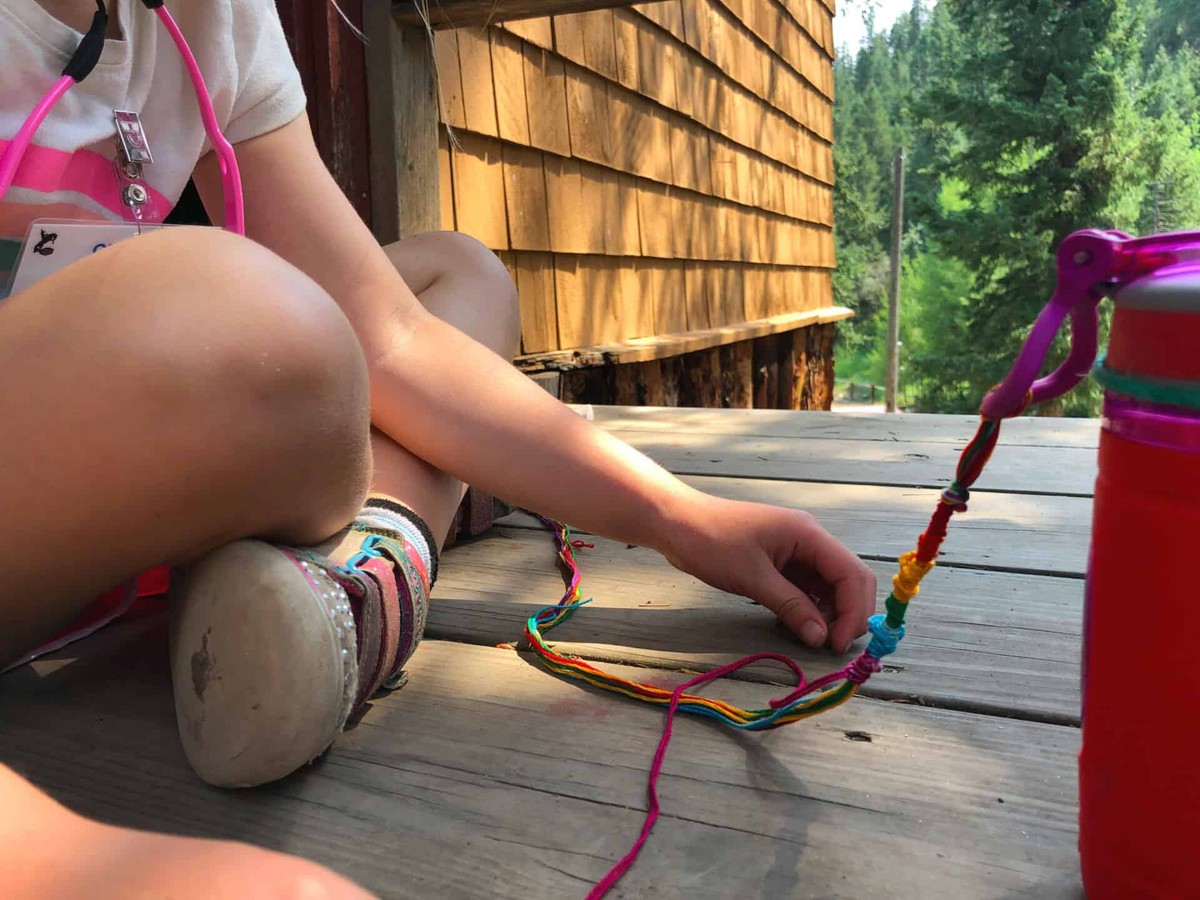 Cheley Family Camp: making a colorful friendship bracelet outside a cabin.