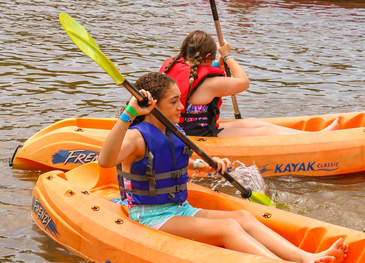 Campers wearing life jackets paddle kayaks on the lake