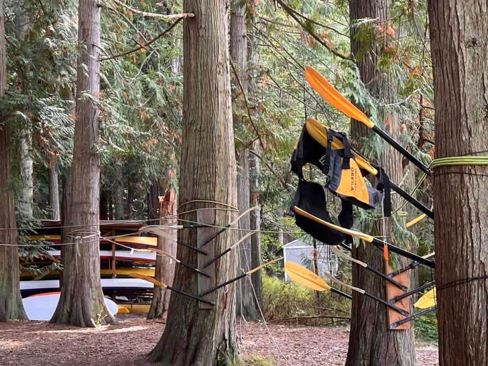 2023 school-trip archive: kayaks, paddles and life jackets stored among the trees at Camp Orkila.