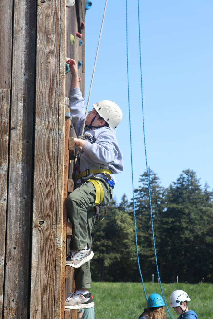 2025 school-trip archive: a student climbs a wooden tower at Camp Orkila using a helmet and harness.