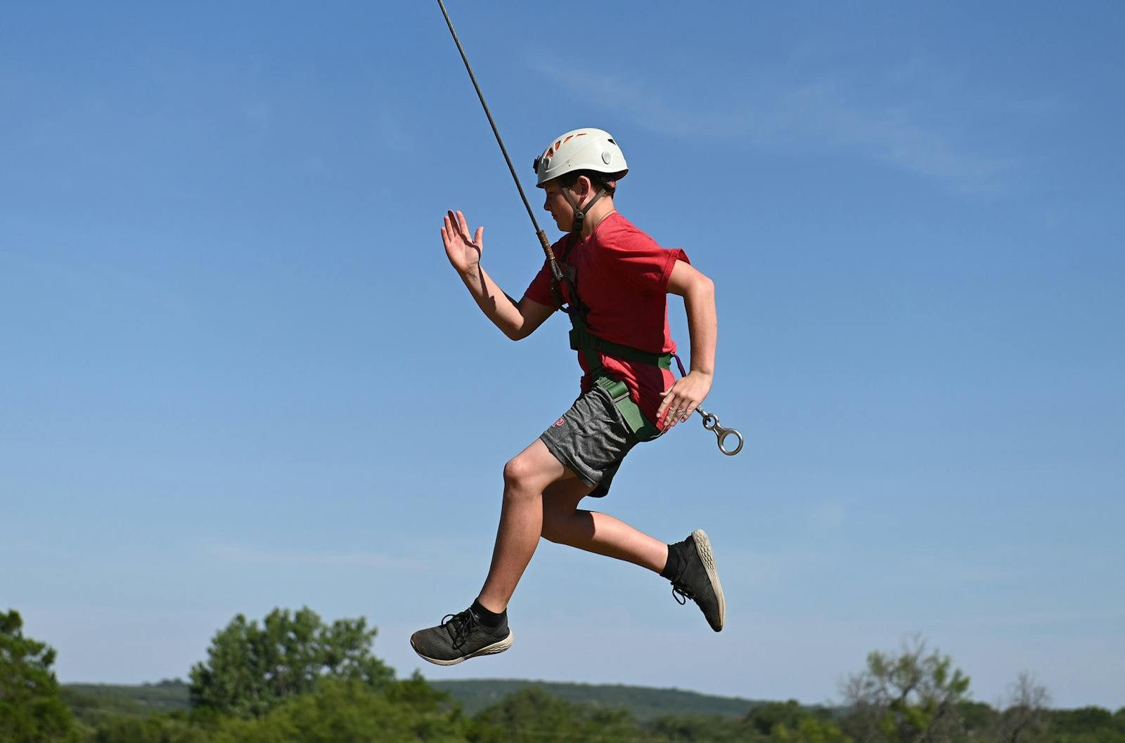 A helmeted camper in a harness jumps through a ropes-course activity