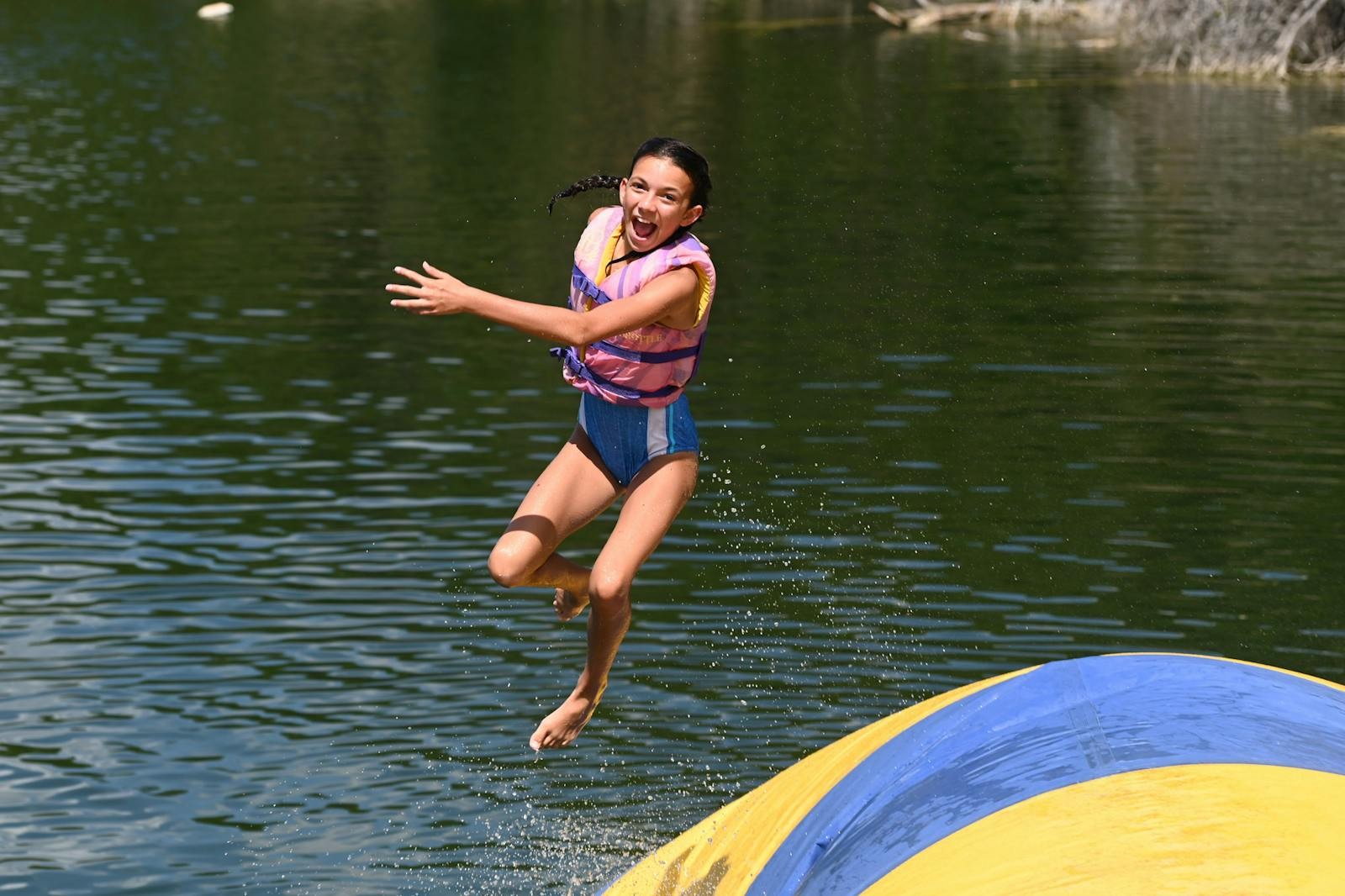 A camper wearing a life jacket bounces above a waterfront inflatable
