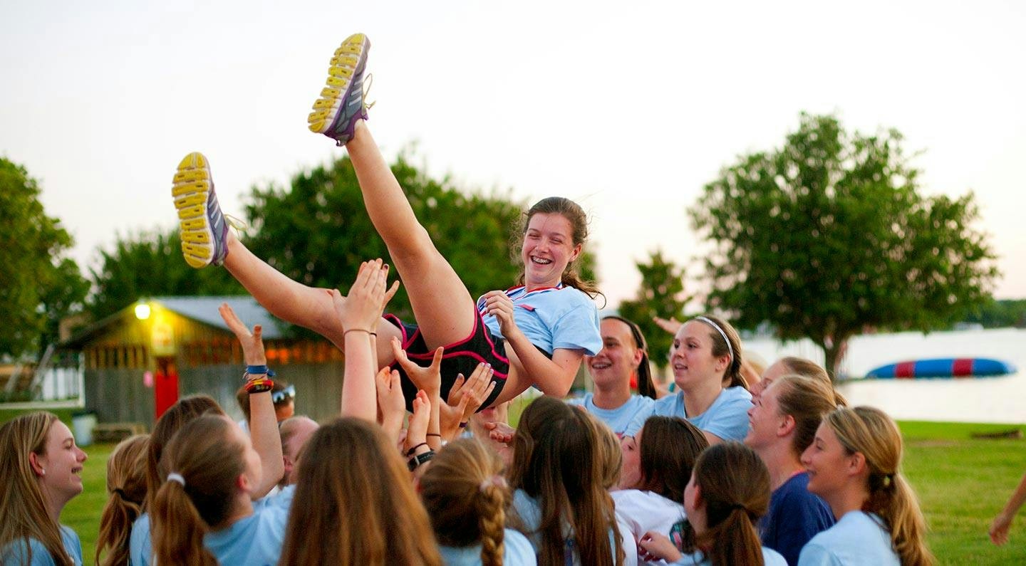 Campers lift a friend together on the lawn