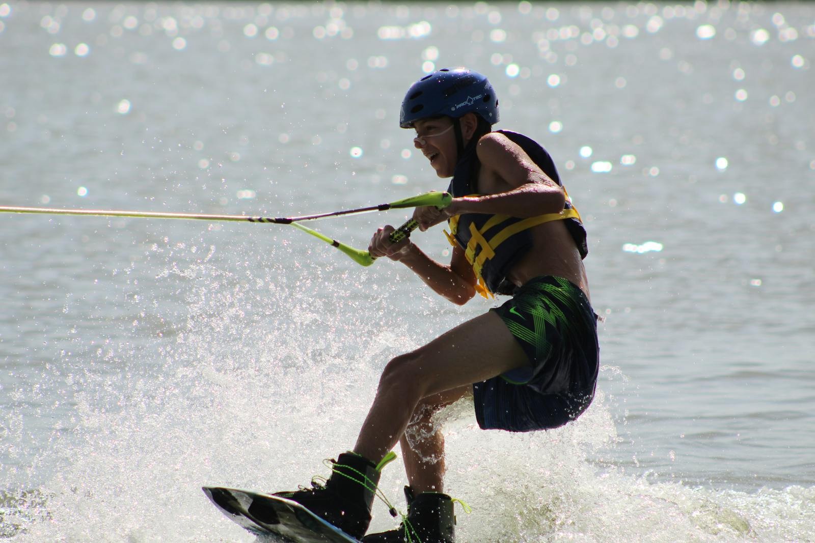 A camper wearing a life jacket wakeboards on the lake