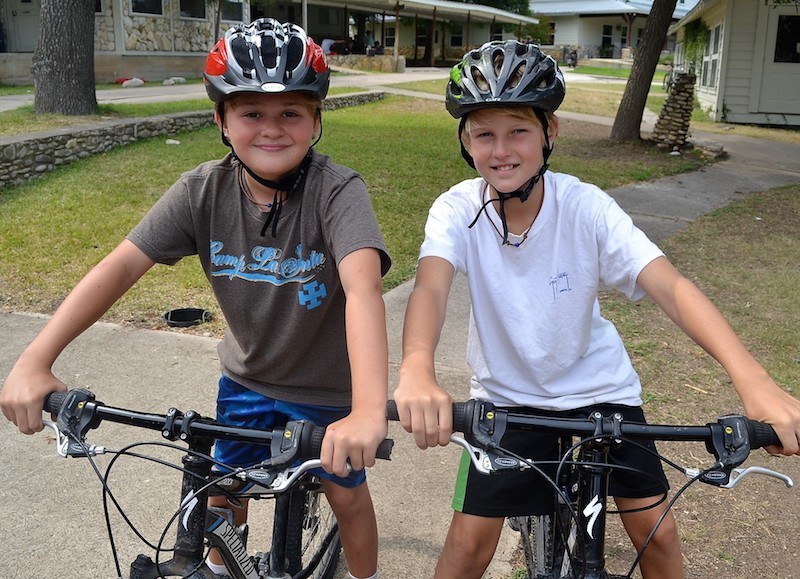 Two helmeted campers stand with bicycles