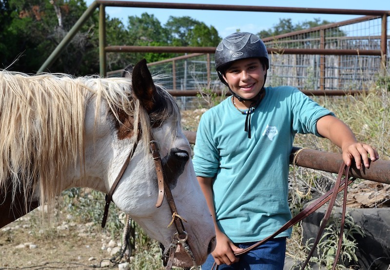 A helmeted camper stands beside a horse