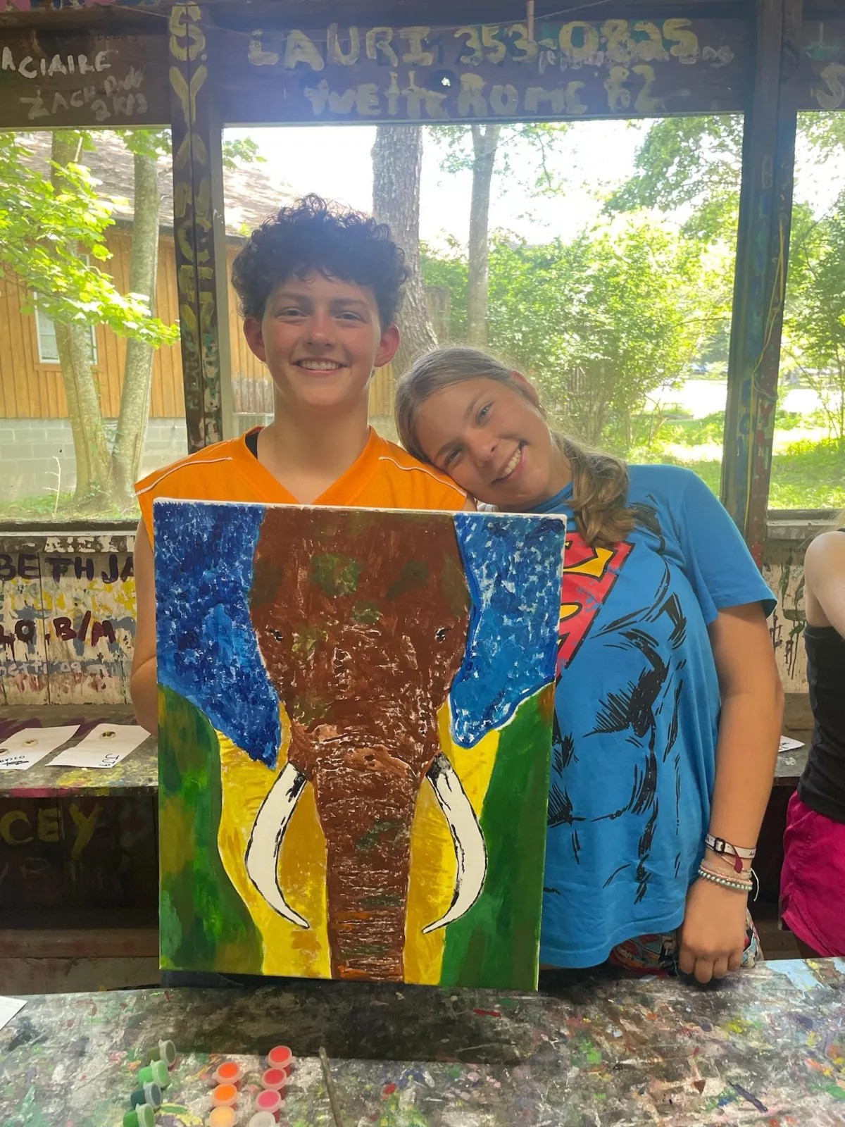 A camper displays an elephant painting in the art area
