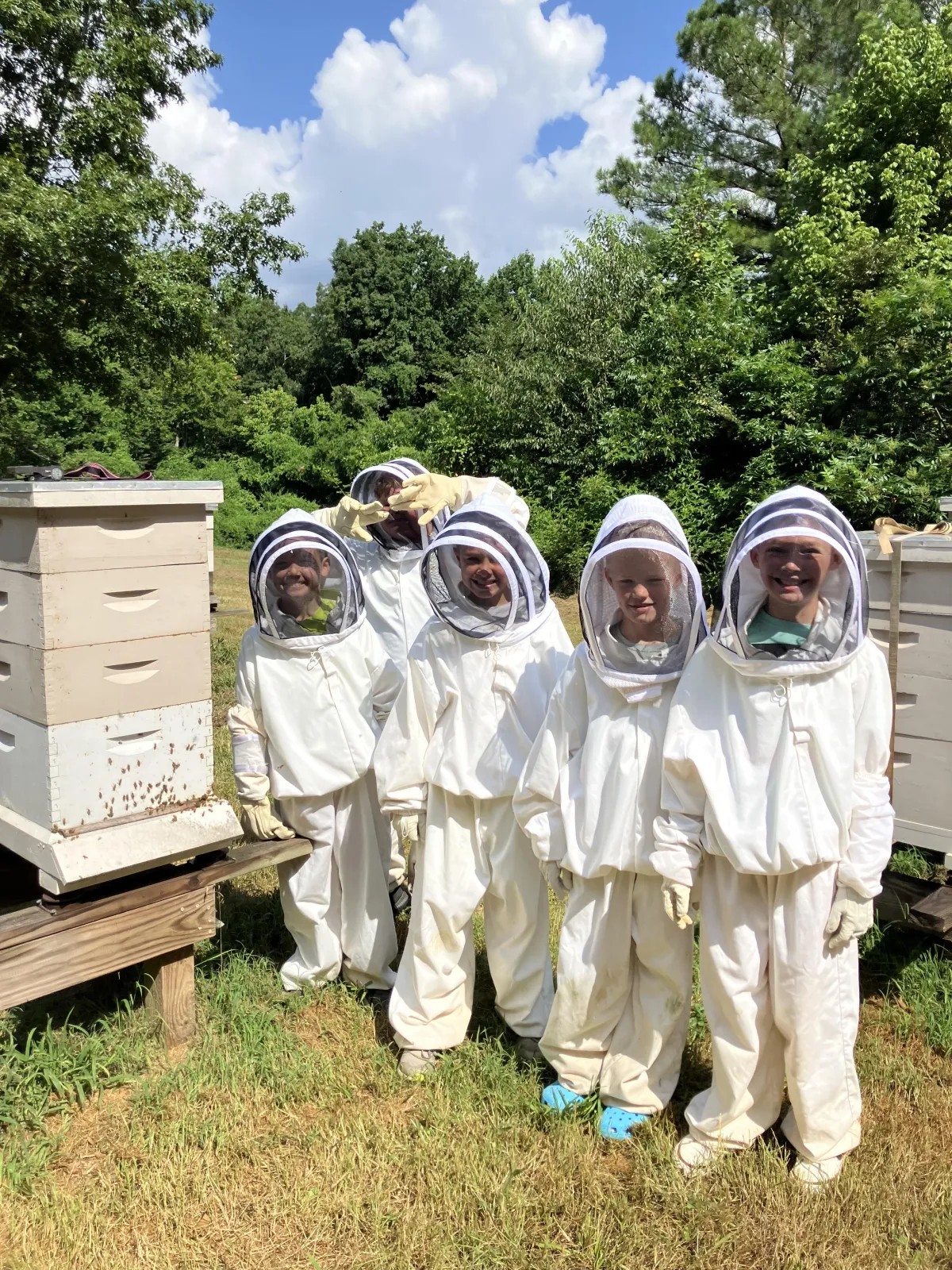 Campers wear beekeeping suits beside beehives