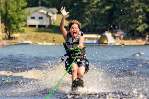 A camper wearing a life jacket waterskis