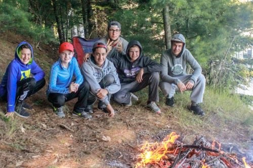 Campers and staff gather beside a campfire in the woods