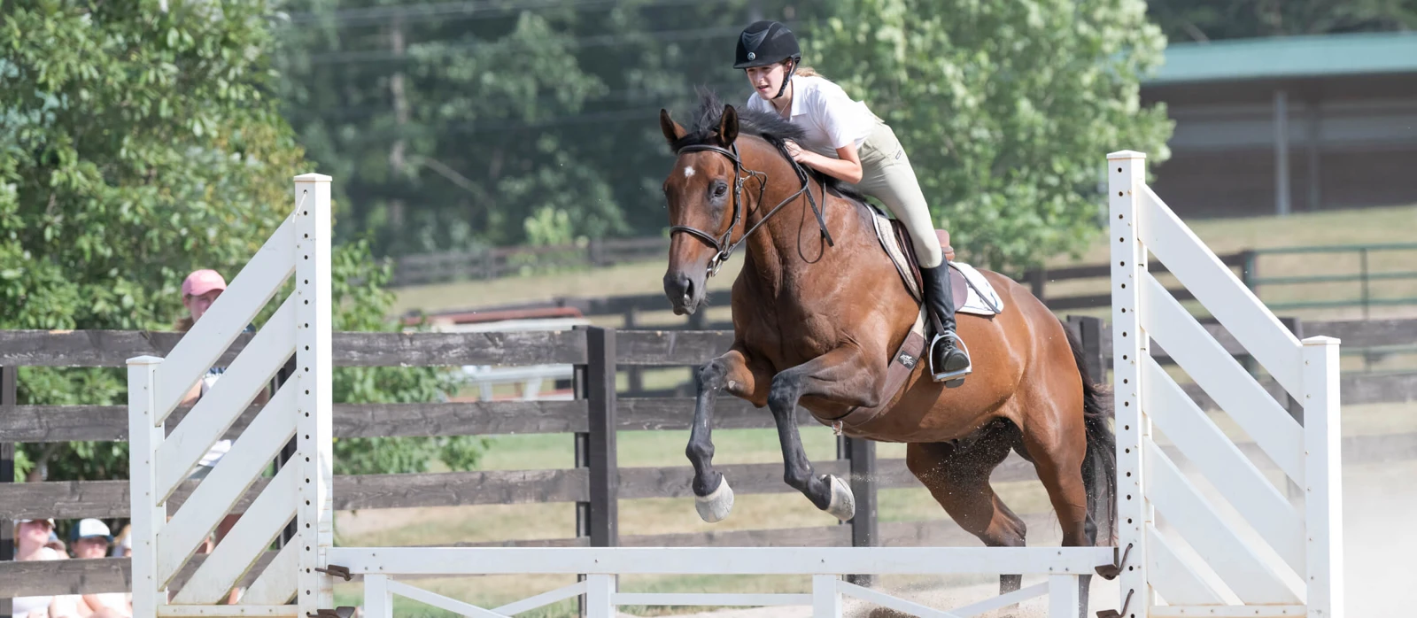 A helmeted rider guides a horse over a jump