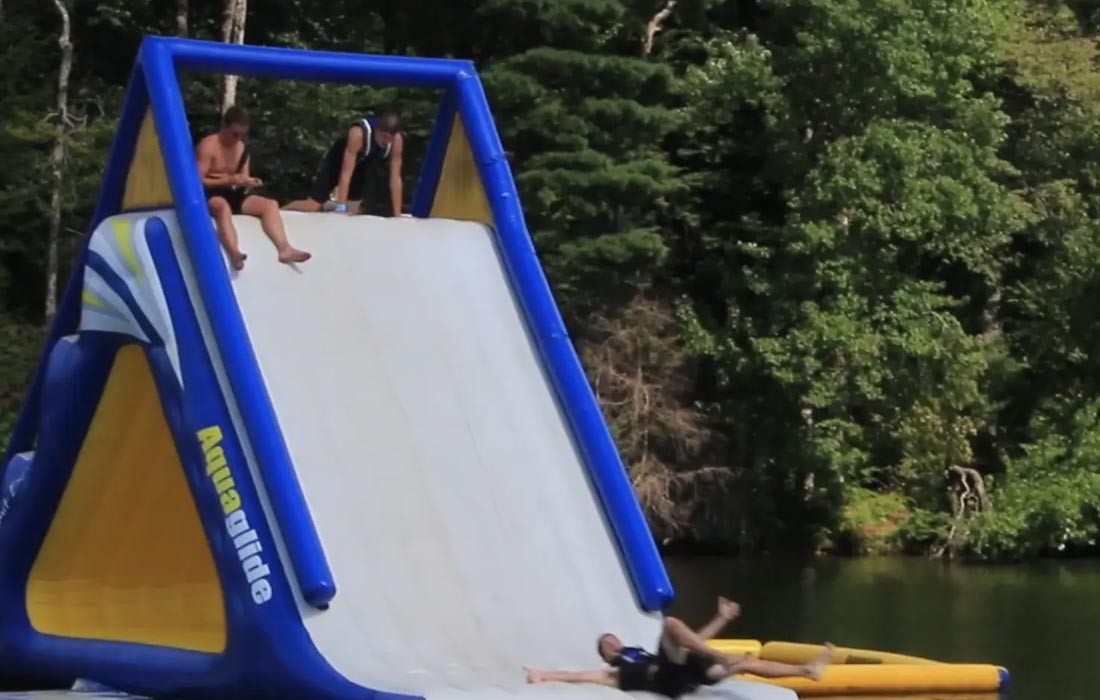 Campers using an inflatable waterslide on the lake