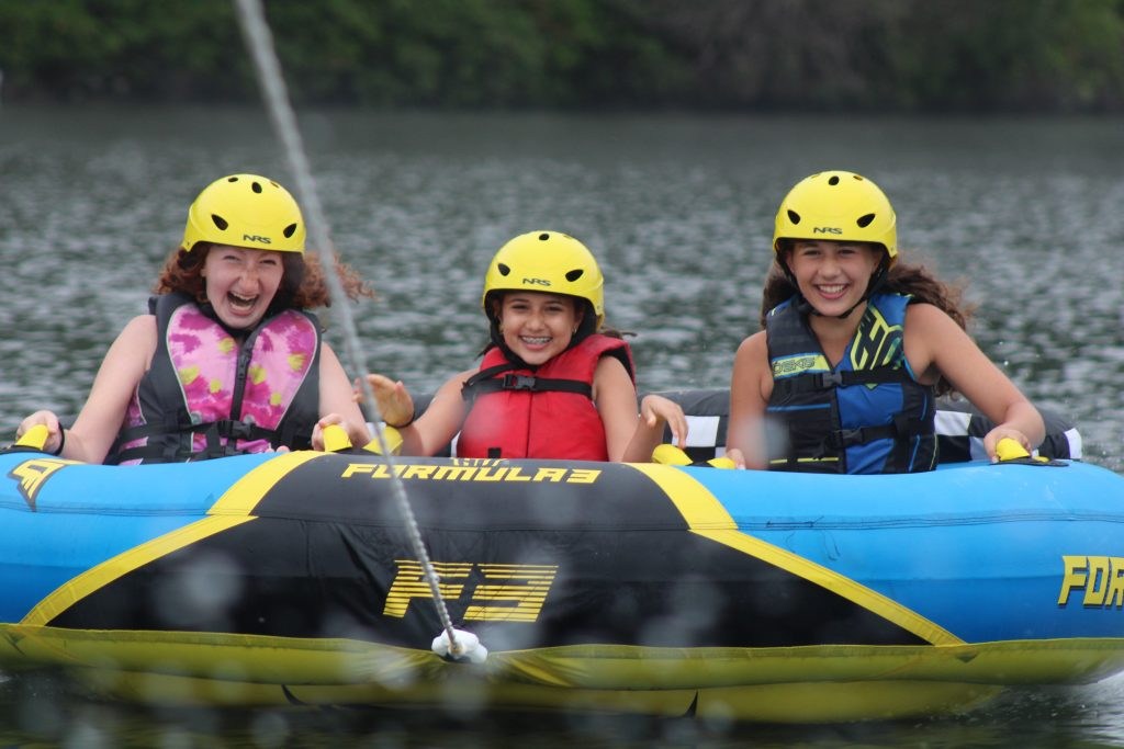 Campers wearing life jackets on an inflatable lake towable