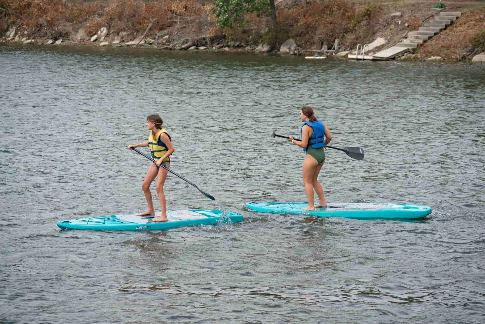 Campers wearing life jackets paddleboard on the lake