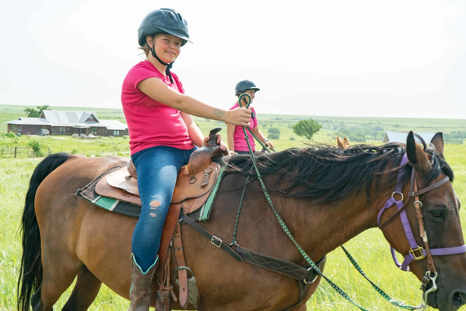 Helmeted campers ride horses on the grassy grounds