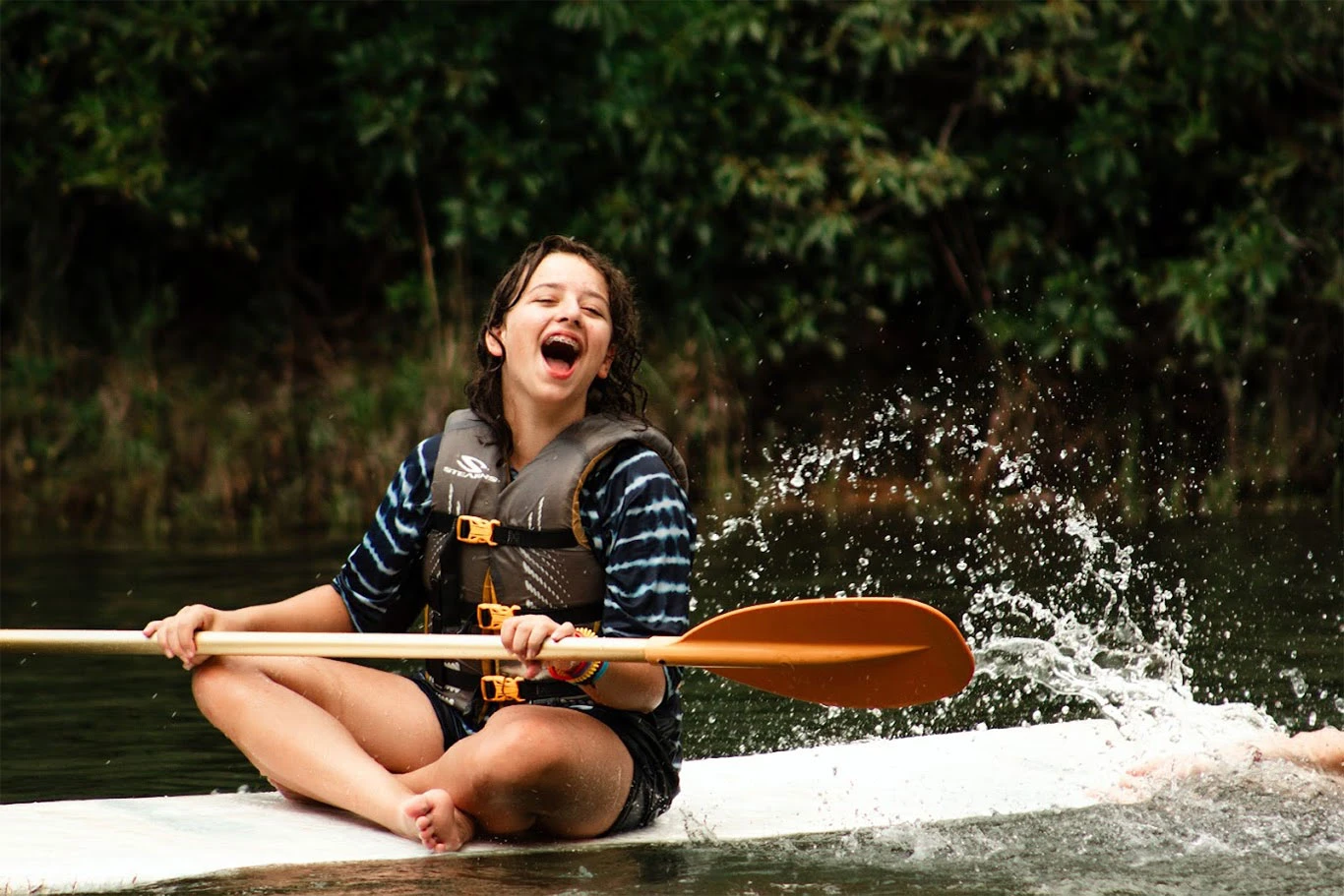 A camper wearing a life jacket paddles on the lake