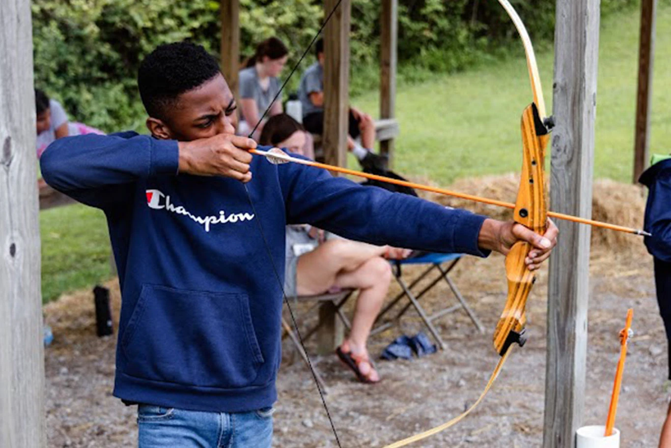 A camper aims a bow at the archery range