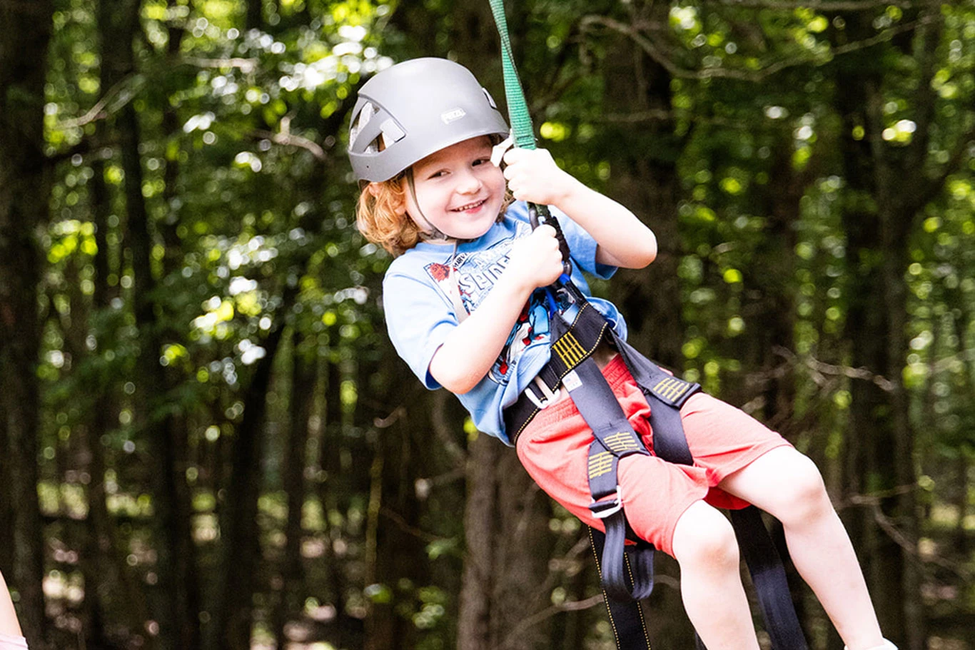 A camper wears a helmet and harness on a zip line