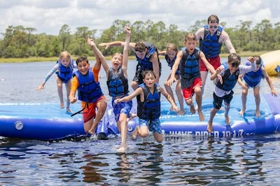 Campers wearing life jackets jump from an inflatable lake platform