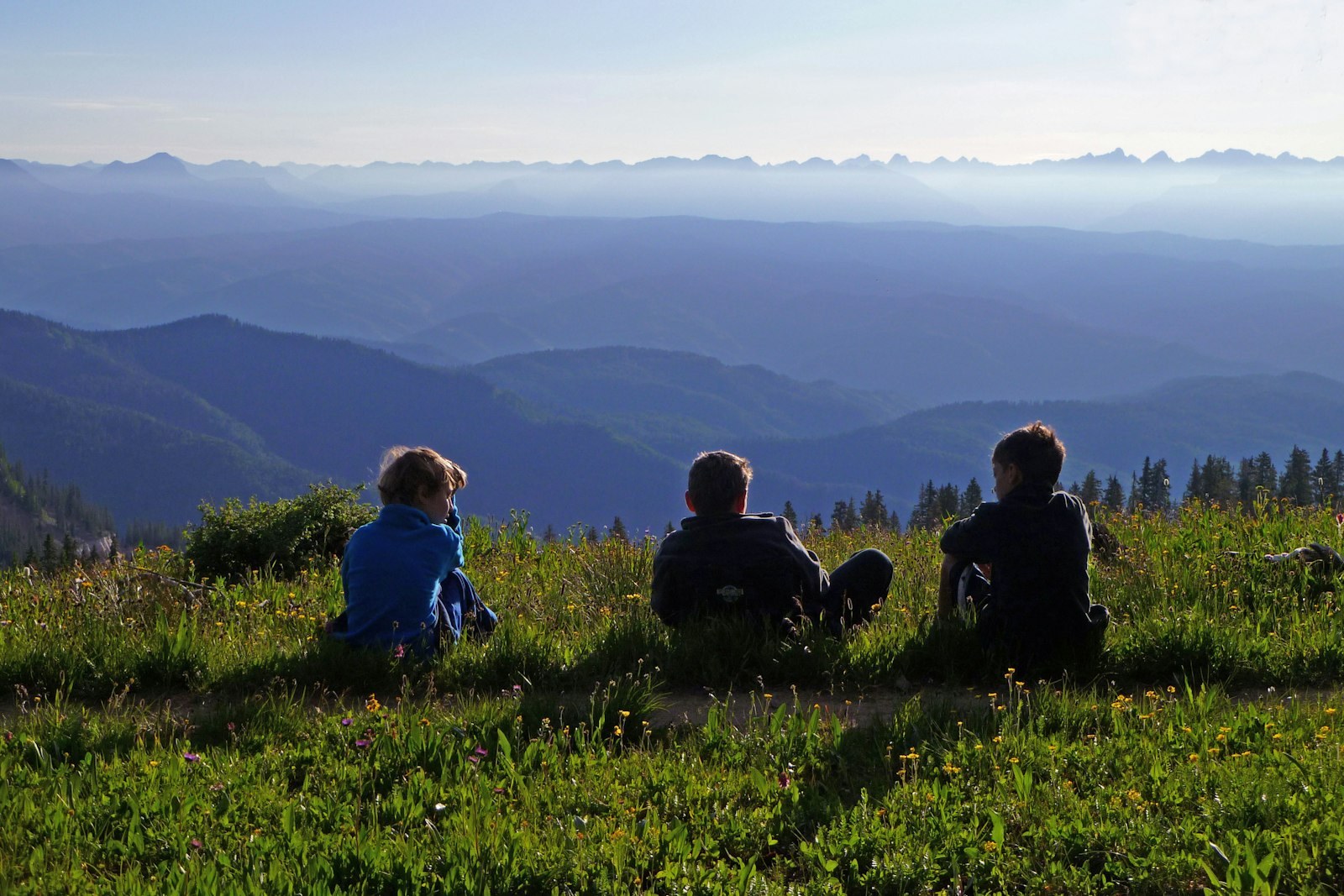 Campers sit in a mountain meadow looking toward distant peaks