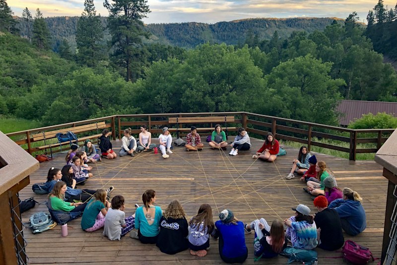 Campers sit in a circle on an outdoor deck