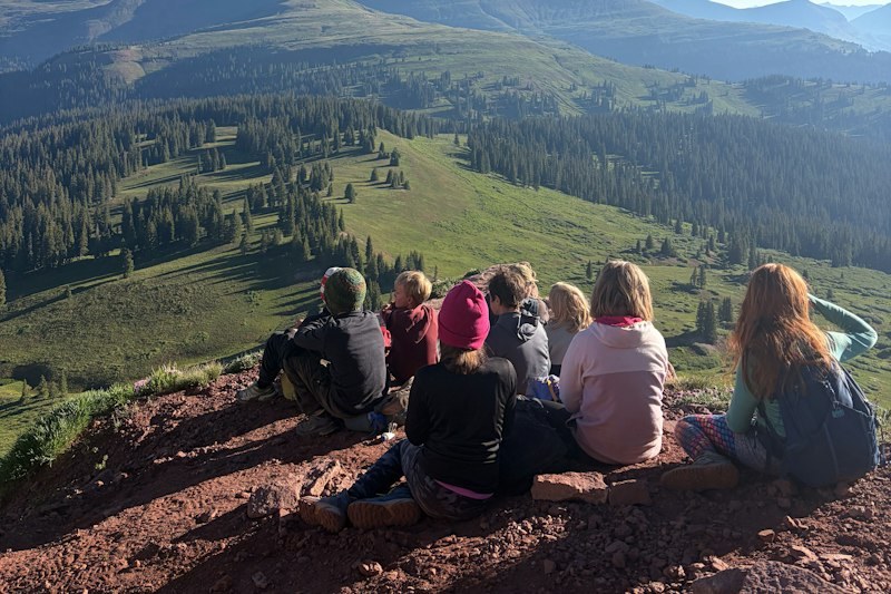 Campers rest on a ridge overlooking forested slopes