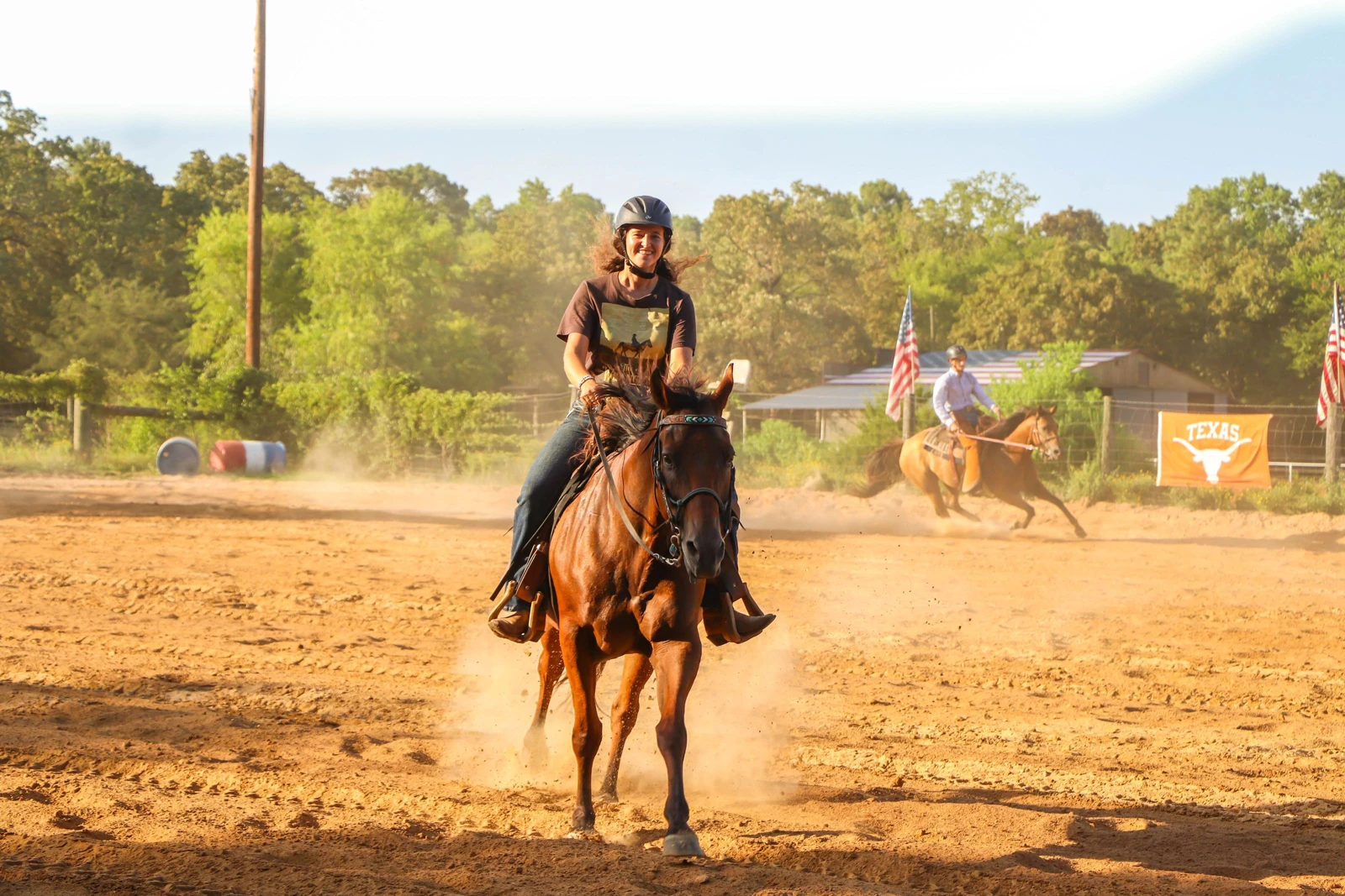 A helmeted camper rides a horse in the riding arena
