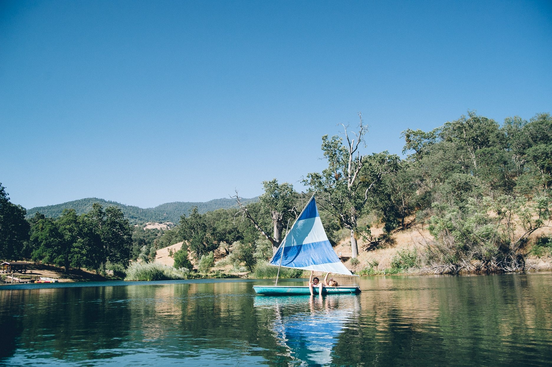 A sailboat on the ranch lake with wooded hills around it