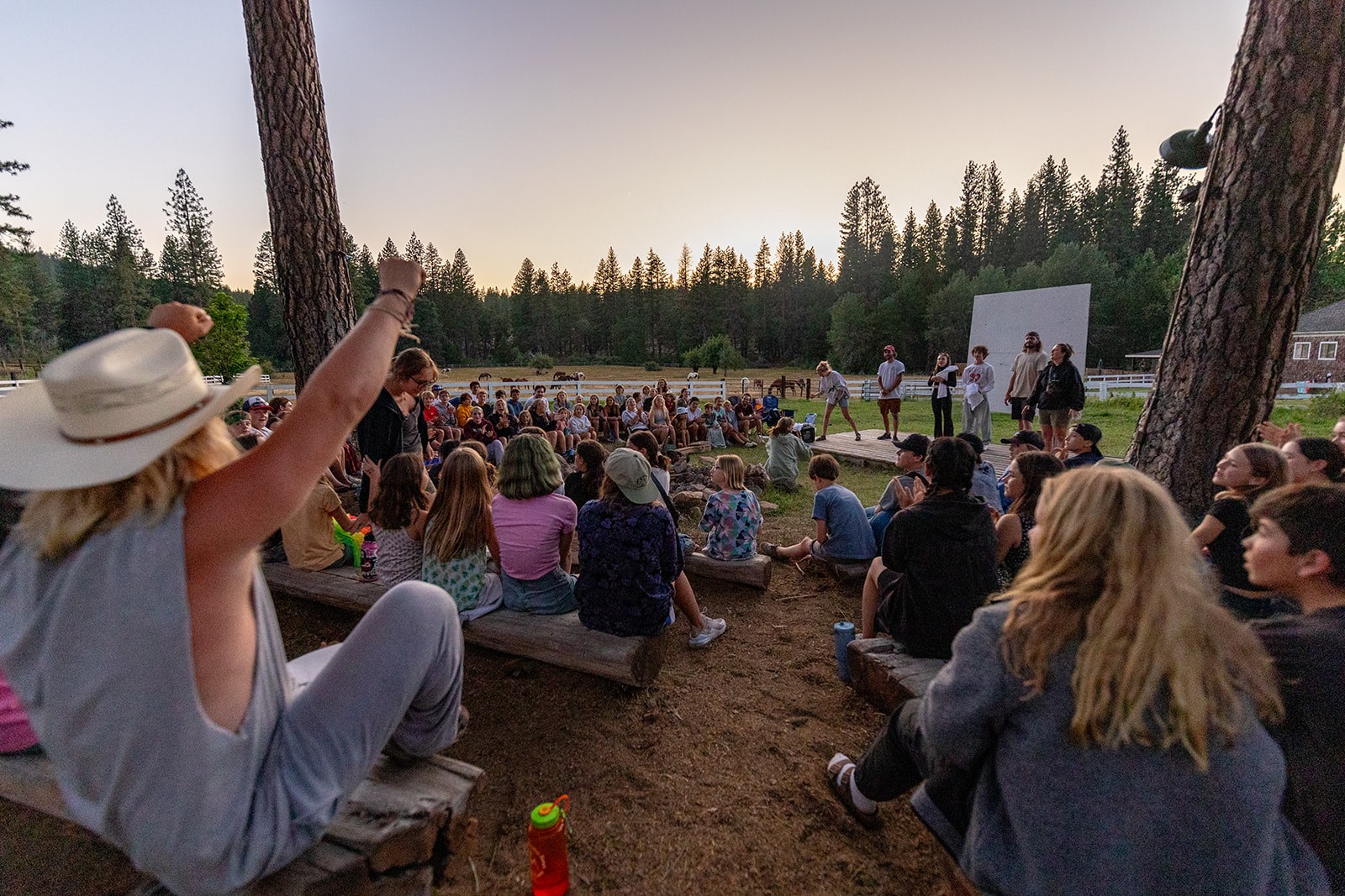 Campers gather among trees for a shared evening activity