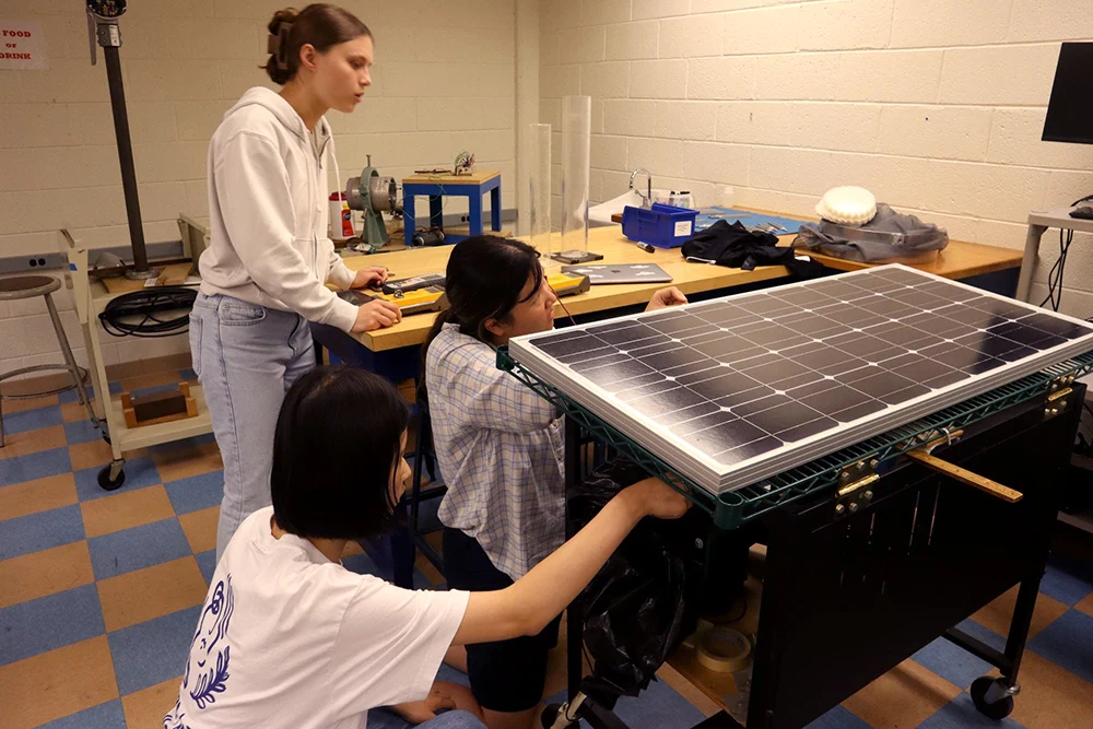 Students examine an experimental setup with a solar panel