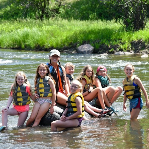 Campers in life jackets gather beside the river