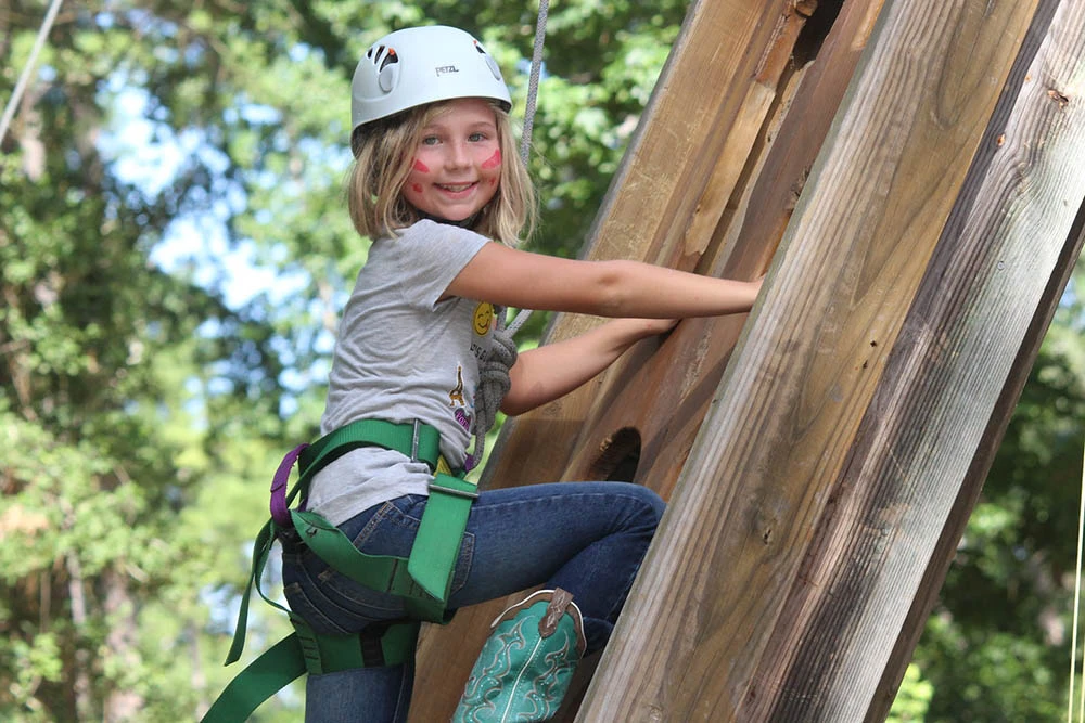 A helmeted camper in a harness climbs the wooden wall