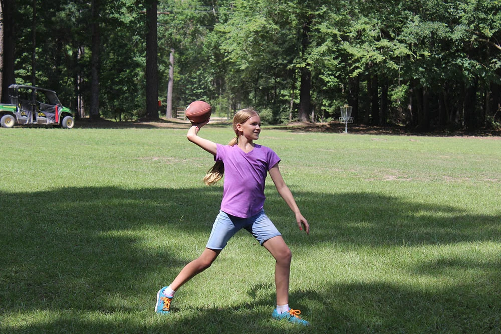 A camper throws a football on the grassy field