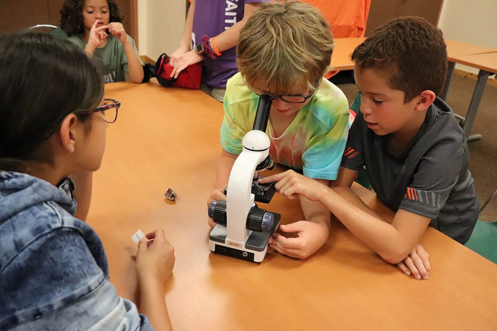 Campers gather around a microscope at an activity table