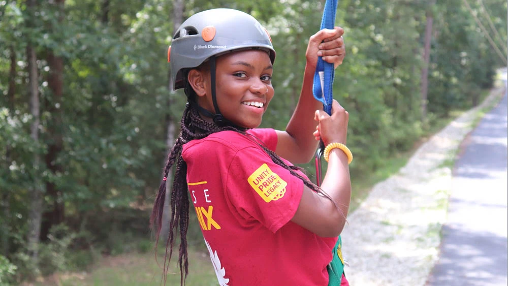 A helmeted camper in a harness tries the zip line