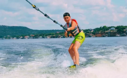 A camper wearing a life jacket rides a wakeboard