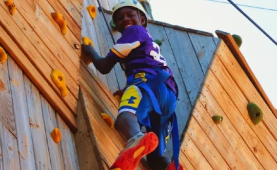 A helmeted camper climbs an outdoor climbing wall